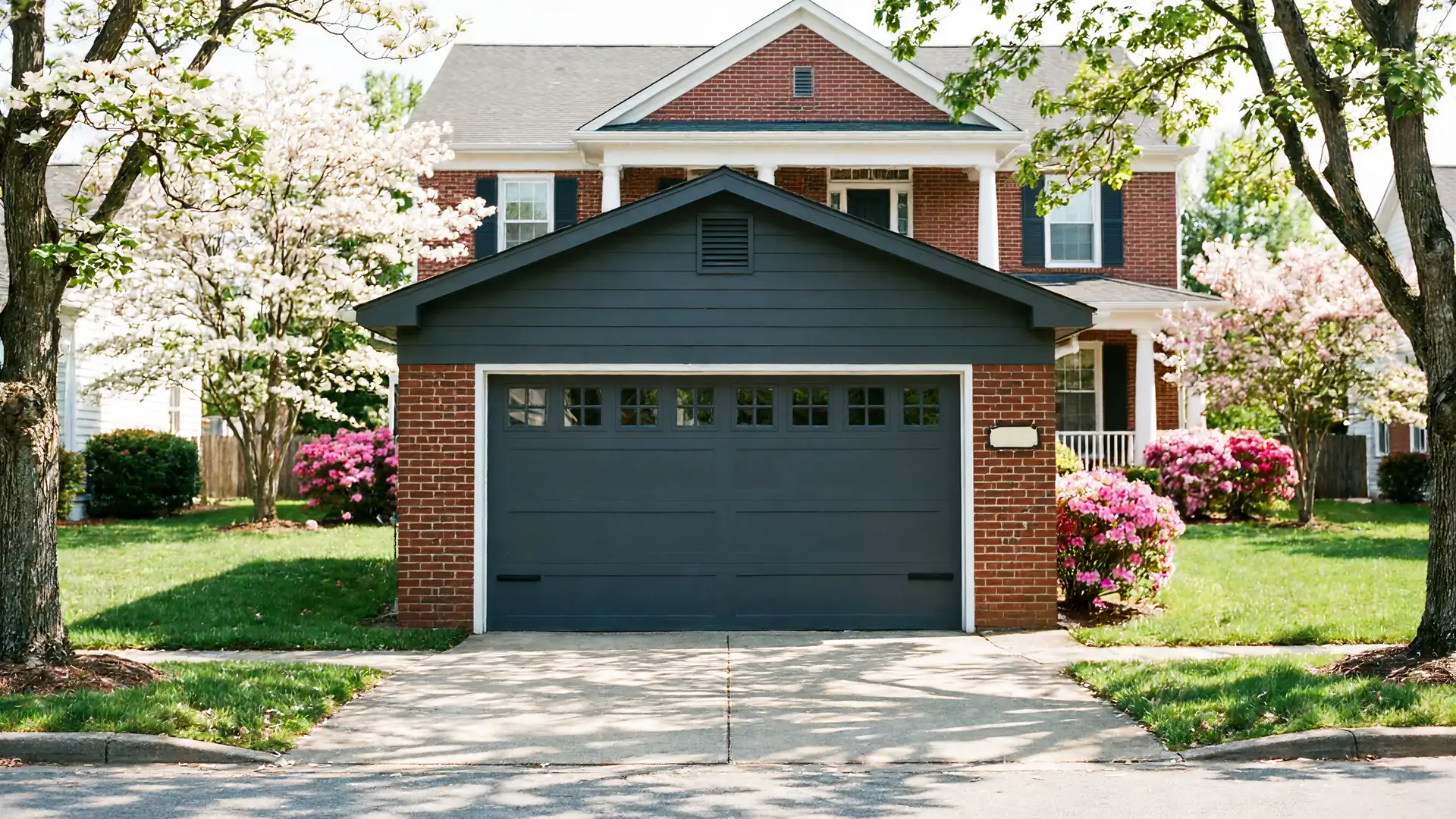 A brick house has a dark gray garage door with windows and a dark gray gable.